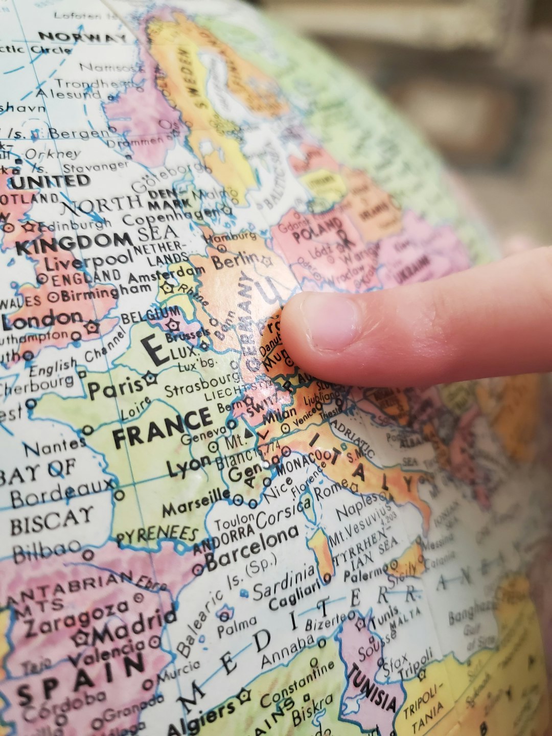 A childs finger points to Germany on a globe. The bright colors of the map has bold black letters indicating places in the world.